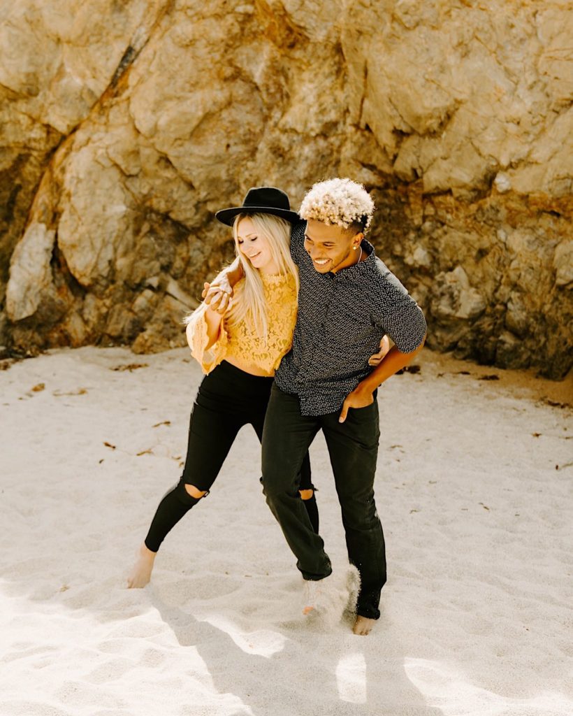 girl and guy walking sillily along garapata beach in big sur