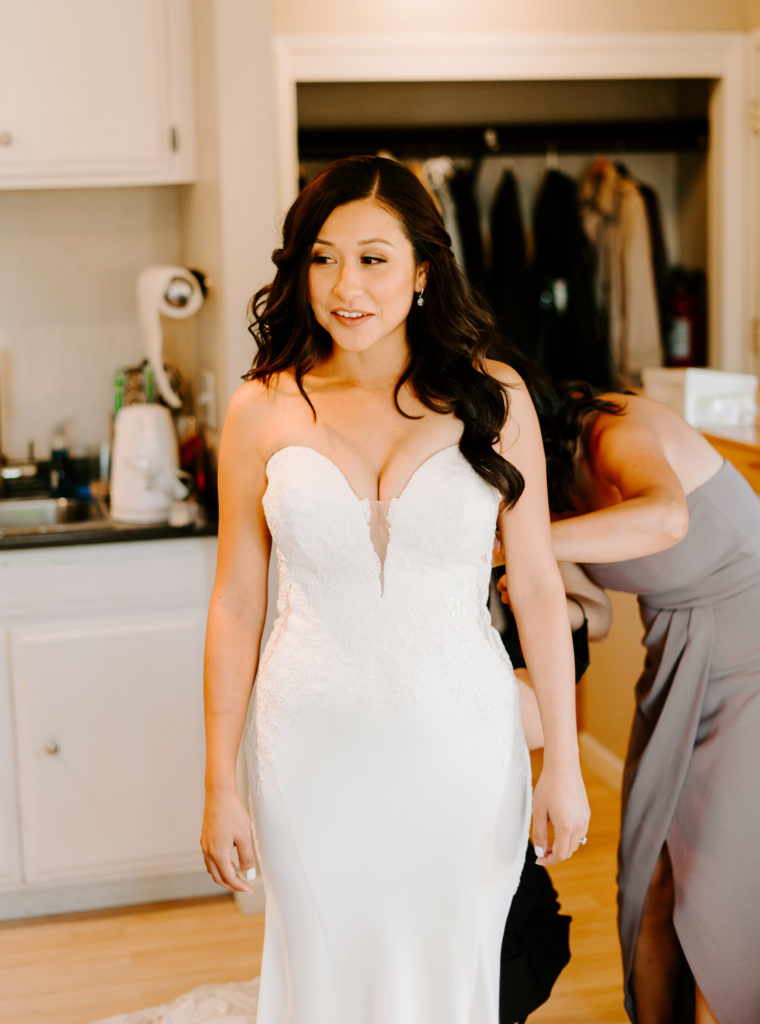 Bride getting buttoned into wedding dress.