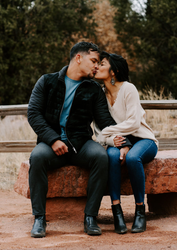 Couple kissing while sitting on rock bench.