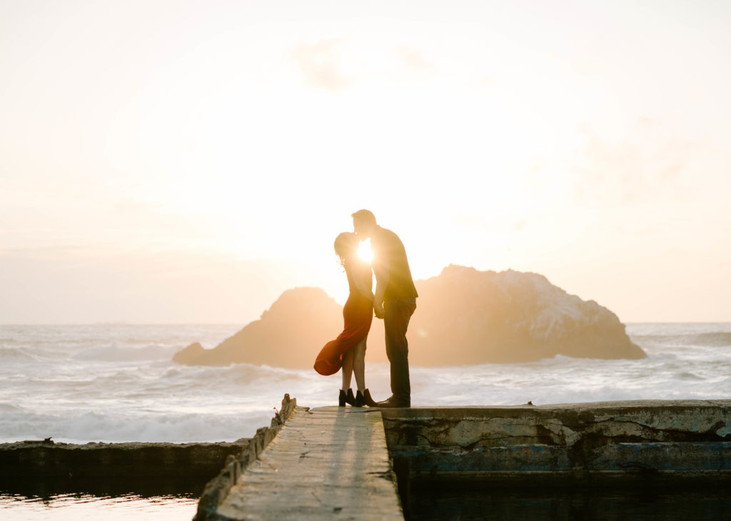Man and woman kissing at Sutro Baths during sunset.