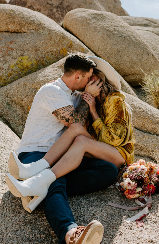 Woman and man kissing while sitting on Jumbo rocks.
