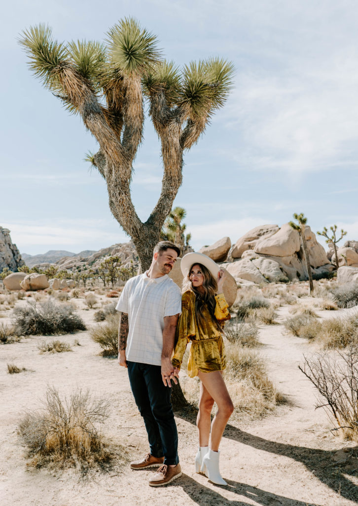 Man and woman looking at each other in front of a Joshua Tree.