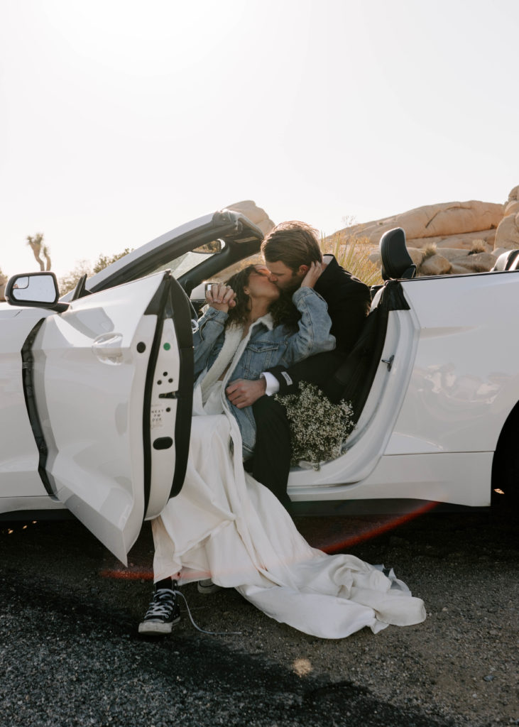 Bride and groom kissing while sitting in front seat of a car.