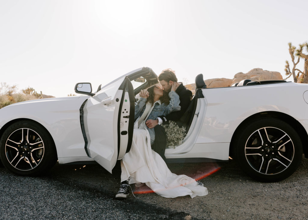 Groom and bride almost kissing while sitting in the front seat of a mustang.