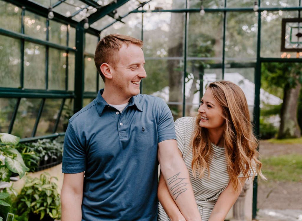Couple bumping hips and smiling in greenhouse.