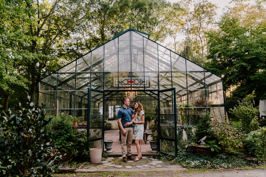 Couple holding each other in front of greenhouse.