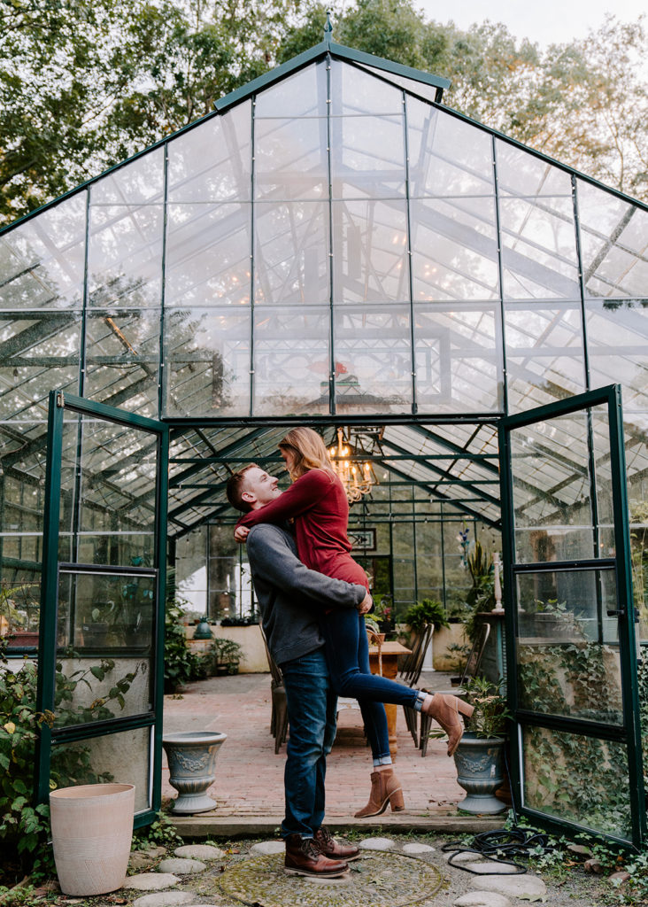 Man picking up woman during greenhouse photoshoot.