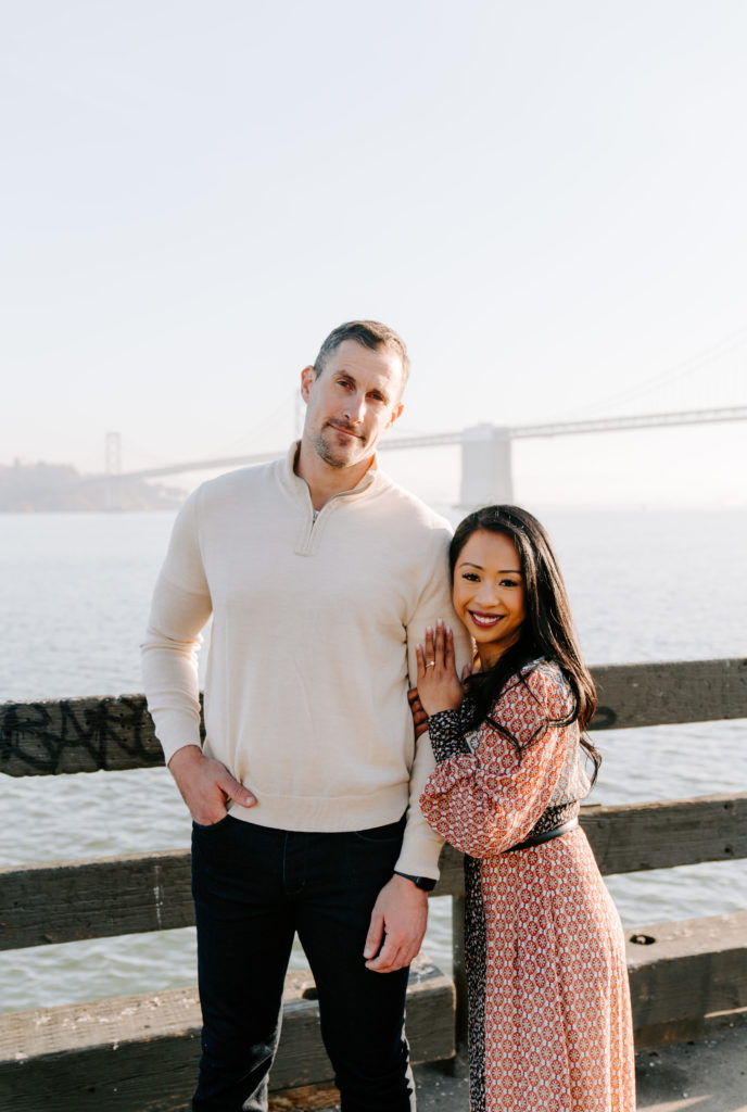 Couple smiling in front of SF Bay Bridge.