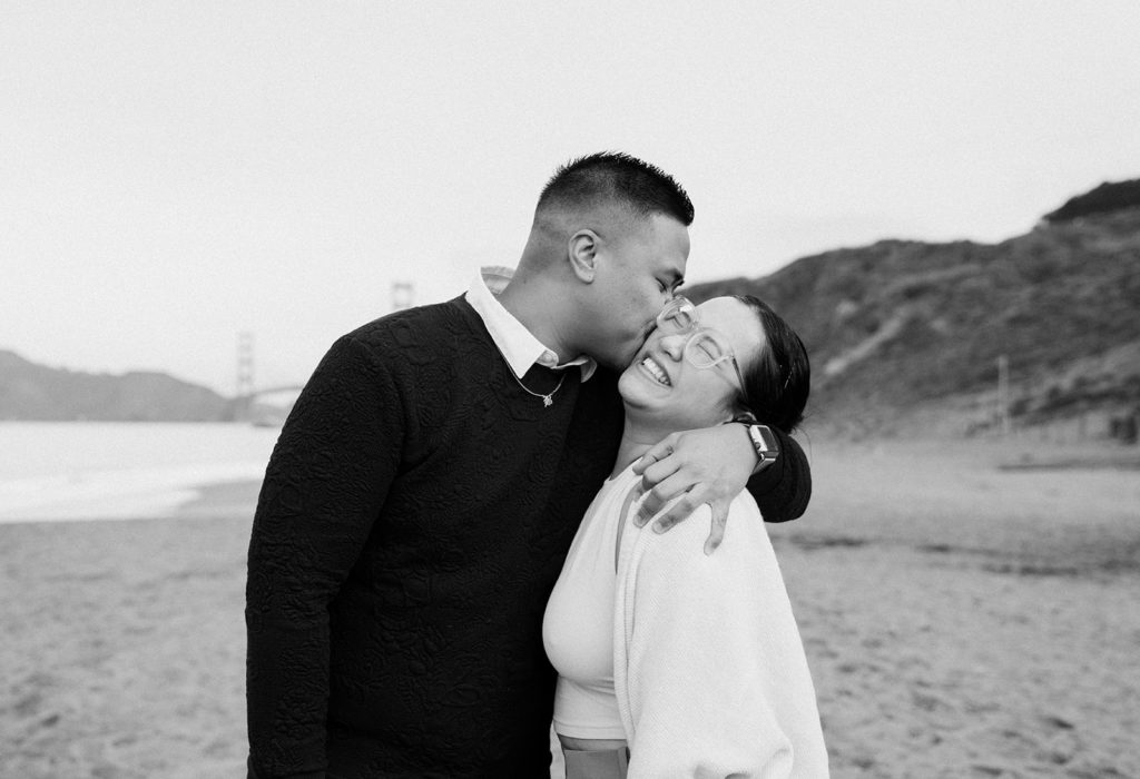 man kissing fiance's cheek baker beach